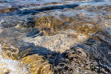 Big stones in seaweed close-up in clear sparkling water. Wild mediterranean sea pebble beach. Rocky shore with sun beam. Travel Greece near Athens. Natural macro patterns