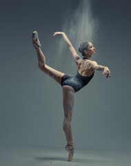 Professional ballerina dancing in studio against gray background - obrazy, fototapety, plakaty