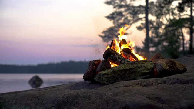 A bonfire burning in a forest on the shore of a lake at midnight on the Summer Solstice. Summer White Night on the eve of Midsummer Day in Finland. Sound of campfire and wildlife, birdsong