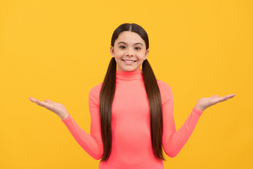 happy teen girl presenting product on copy space on yellow background, choice
