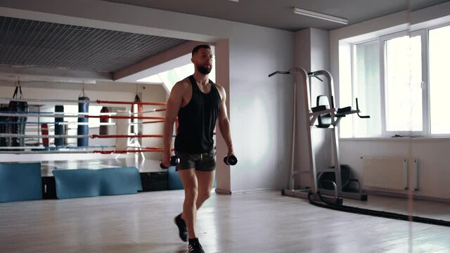 Attractive, muscular young man, equipped in a sporty form, performs lunges with 3 kilogram dumbbells in the gym. Healthy lifestyle. Sport concept