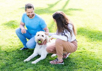 young family of man and woman play with dog pet in park on green grass, pet lover