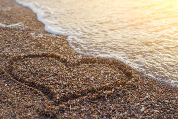 Heart on a sand of beach with wave on background.