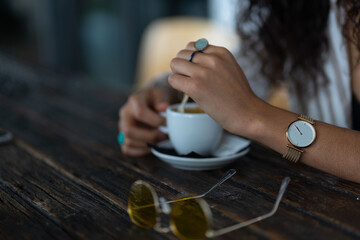 woman with rings and watch having a cup of coffee at wooden table