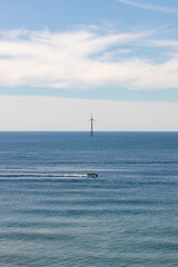 Fototapeta premium A fishing boat passing in front of a wind turbine on the ocean