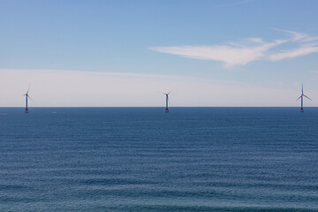 Three wind turbines out on the horizon and on a calm ocean