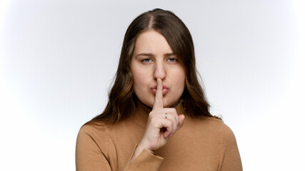 Naklejka premium Studio portrait of young woman holding finger at mouth and saying shhh. Concept of keeping secret and silence
