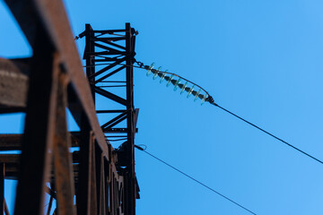 Rusted steel power transmission tower in Ukraine with high-voltage lines and insulators, symbolizing aging Soviet-era infrastructure still in use, set against a clear blue sky.
