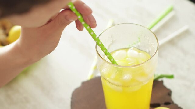 Yellow soda with ice in a tall glass. A girl without a face quenches her thirst, drinks a cocktail through a cocktail tube. A large glass of chilled tropical drink with a paper straw on a hot day.
