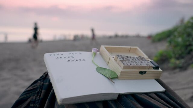 A scrapbooking journal of a female sitting on the sand with the words 'Find Your Inner Peace' written on a page with a vintage style stamping wooden set and a flower on a beach after sunset. Harmony.