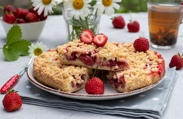 Italian sbricholata pie with shortcrust pastry and strawberries on a gray table with a bouquet of daisies. Still life in an open space