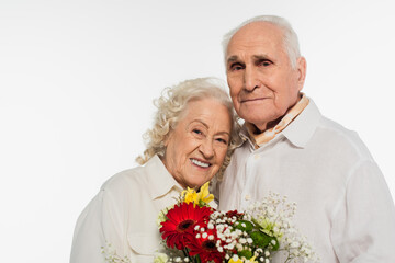happy elderly couple holding bouquet of flowers and looking at camera isolated on white
