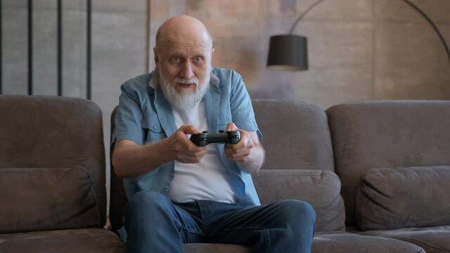 Portrait of happy cheerful bearded elderly retired grandfather emotionally playing video game on console holding controller, emotions of joy from defeat and victory in video game.