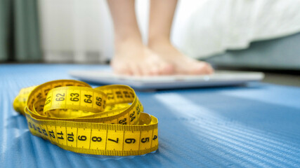 Measuring tape, fitness mat and young woman weighting on scales. Concept of dieting, sports, loosing weight and healthy lifestyle.
