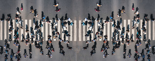 Different people at a pedestrian crossing in the city - panorama shot. People at a zebra pedestrian crossing - a lot of pedestrians in an overcrowded city on a sunny day. Aerial drone banner shot. 