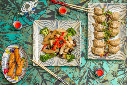 Top view image of Asian food dishes, shrimp rolls, steamed gyozas and rice pasta with vegetables and shiitake mushrooms