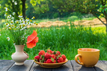 Fototapeta na wymiar Summer still life of a plate with strawberries and coffee on a table with flowers. Summer morning or evening background