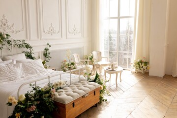white bed by the large bedroom window. the bed is decorated with flowers. bedroom with large bed