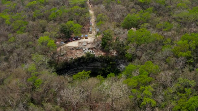 Forwards tilt-down reveal of large round Cenote sinkhole in ground. Sun reflecting on water surface. Historical monuments of pre-Columbian era, Chichen Itza, Mexico.