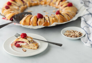 A freshly baked raspberry crescent ring with a slice out in front ready for eating.