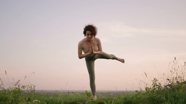 In slow motion, a young woman performs yoga exercises by performing balancing and stretching on top. Calm and peaceful balance of body and soul. Body bends and bends