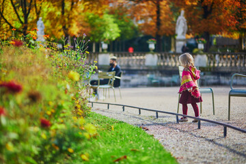 Adorable little girl in pink knitted poncho walking in Luxembourg garden