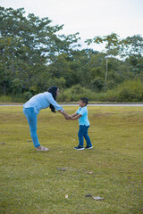 mom holding hands of her son joyful in the green field