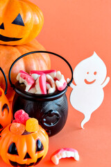 Happy Halloween decoration. Pumpkin, cauldron, skull and gummy candies on orange background.