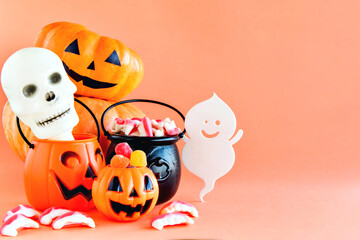 Happy Halloween decoration. Pumpkin, cauldron, skull and gummy candies on orange background.