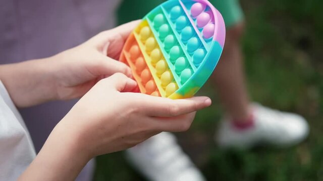 Close up bunner shot of hands unrecognizable kid holding rainbow Pop It fidget toy in hands. Teen Playing, Push soft silicone bubble. Popular trend 2021. anti stress toy. slow motion. 