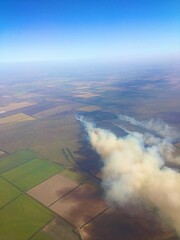 The smoke from the fire rises to the sky and is visible from a height from the window of an airplane taking off.