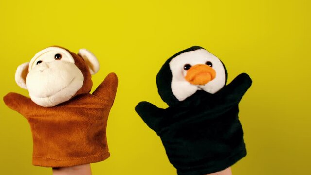 Soft puppet toys on hands on yellow background. Concept of puppet show. Close-up of hands with puppet monkey and penguin.