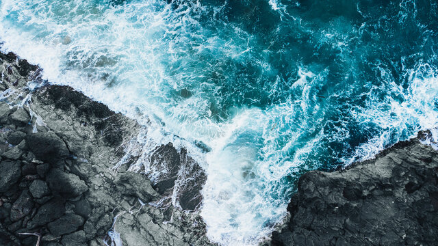 Drone shot of ocean waves clashing into dark rocks