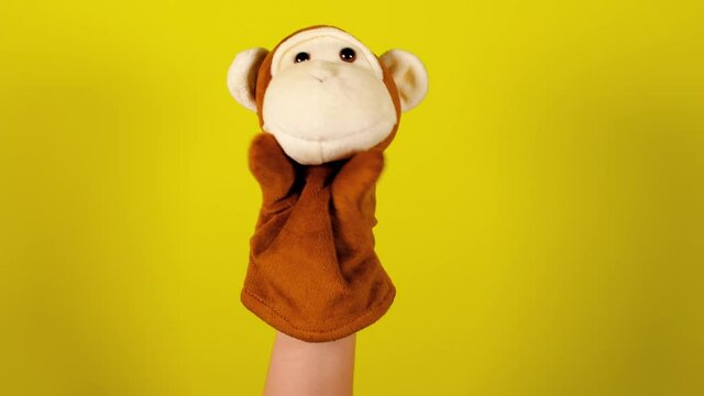 Soft puppet toy on hand on yellow background. Concept of puppet show. Close-up of hand with puppet monkey