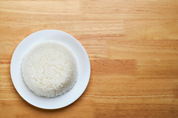 flat lay top view shot of streamed white Thai's jasmine rice in the white clean dish isolated put on the wooden plate dinner table closed to one conner of the photo with empty copy space for texts