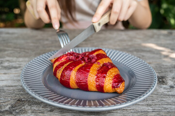 Close up of woman trying to eat Raspberry Croissant with knife and fork. Croissant is a French buttery, flaky and crescent-shaped bread.