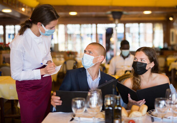 Fototapeta na wymiar Woman waiter in protective mask is taking order from clients in restaurante indoor