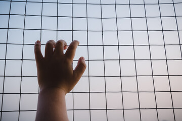 Little boy hand holding on chain link fence for freedom with dark feeling. concept of the freedom