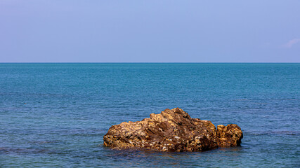 Orange brown rocks with calm sea waves during a sunny day at a tropical rocky beach. Rocky island, a destination for tourists in summer time