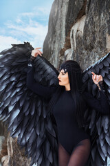 beautiful young brunette woman with long black hair in a black angel costume on a rock background
