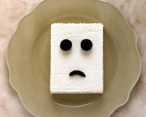 tofu block with a sad expression made of olives on a brown plate