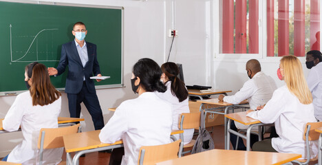 Confident male speaker in protective face mask lecturing to medicals during training meeting