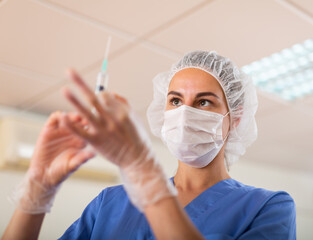 Young nurse in the treatment room prepares a syringe for injection, filling in with medicine