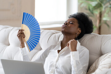 Tired Afro business woman suffering from heatstroke or hot summer flat without air-conditioner,...