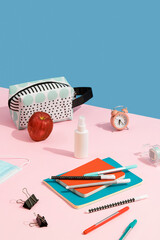 Alarm clock, colorful notepads, pens and hand sanitizer on pink table with copy space