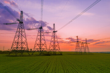 high voltage lines and power pylons in a green agricultural field against a saturated sunset sky