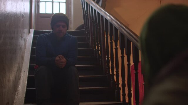 The two men meet on the stairs of an old house. Communication of neighbours of an apartment building. The man sits down on the step.