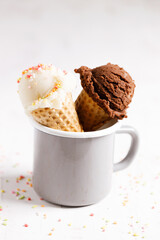 Ice cream scoops in cones on white wooden background.