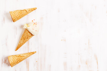 Ice cream scoops in cones on white wooden background.