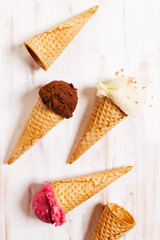Ice cream scoops in cones on white wooden background.